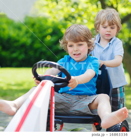 Two funny little boys having fun with race car outdoors 16863336