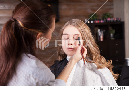 Stylist doing professional make up of young woman 16890433