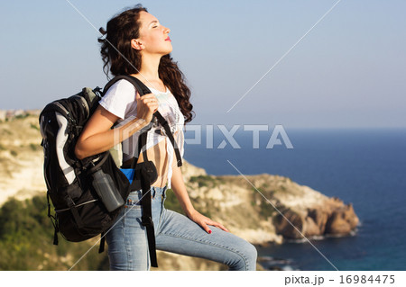 Girl traveler is standing on rock with backpack Girl traveler is standing on rock with backpack 16984475