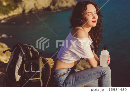 Happy girl backpacker is sitting on rock over sea view Happy girl backpacker is sitting on rock over sea view 16984480
