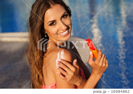 Smiling girl applying sunscreen lotion on her shoulders Smiling girl applying sunscreen lotion on her shoulders 16984862