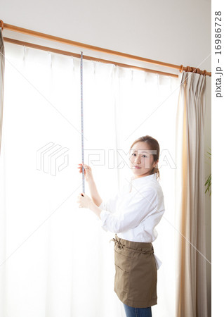窓のカーテンのサイズを測る女性 16986728