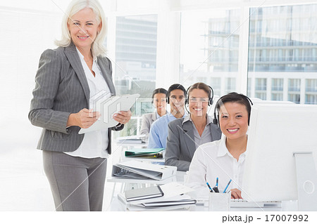 Smiling businesswoman looking at camera while work team using co 17007992