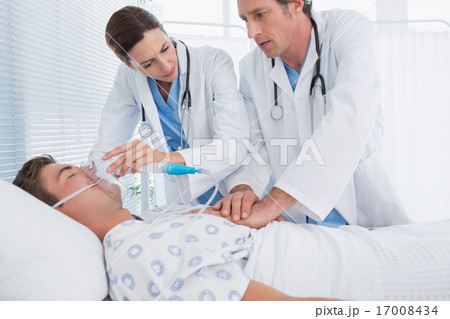 Worried doctors doing heart massage and holding oxygen mask 17008434