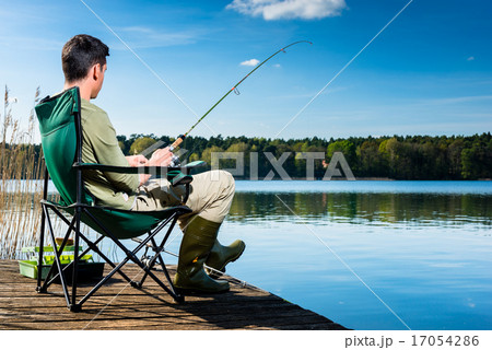 Man fishing at lake sitting on jetty 17054286
