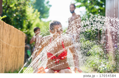 Family cooling down with sprinkler in garden 17054584