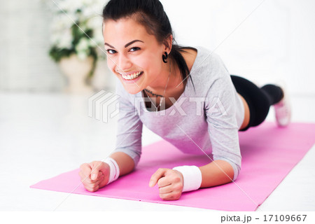 Pretty smiling young woman doing plank abdominal exercise at home in white room looking camera 17109667