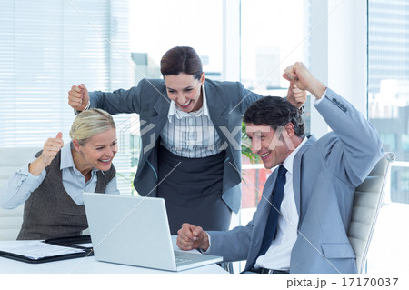Business people cheering in front of laptop at office Business people cheering in front of laptop at office 17170037