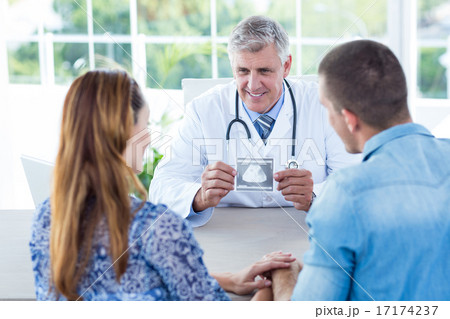 Smiling doctor showing ultrasound scan to the couple Smiling doctor showing ultrasound scan to the couple 17174237