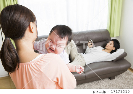育児イメージ　泣く赤ちゃんをあやすお母さんとソファでスマホをいじるお父さん 17175519