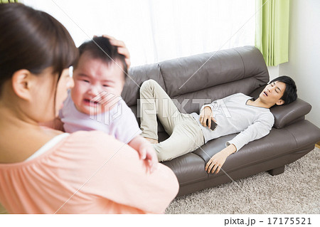 育児イメージ　泣く赤ちゃんをあやすお母さんとソファでスマホをいじるお父さん 17175521