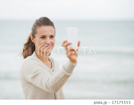 Happy young woman in sweater on beach taking photo using cell ph Happy young woman in sweater on beach taking photo using cell ph 17175553
