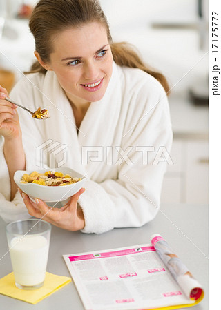 Thoughtful young woman in bathrobe eating breakfast in kitchen 17175772