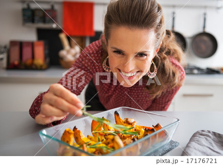 Happy young housewife adding rosmarinus to baked pumpkin 17176721