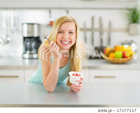 Happy young woman eating yogurt in kitchen 17177117