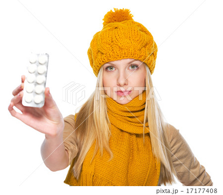 Serious girl in scarf and hat showing blister package of pills 17177408
