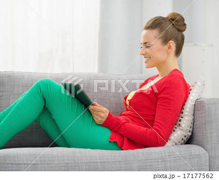 Smiling young woman sitting on divan and using tablet pc 17177562