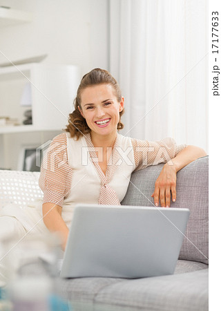 Smiling young woman sitting on sofa in living room with laptop 17177633