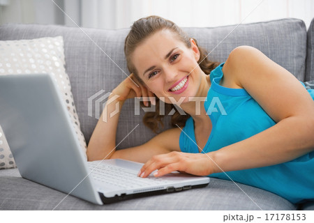 Smiling young woman laying on sofa with laptop 17178153