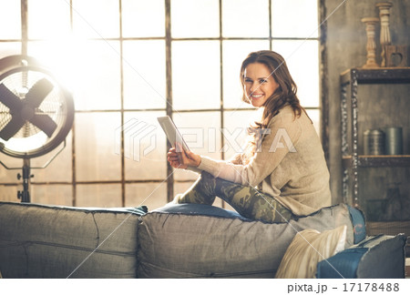 Smiling woman sitting on back of sofa looking up from table pc 17178488