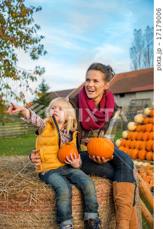 Happy mother and child sitting on haystack with pumpkins and poi 17179006