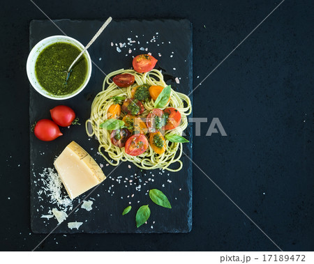 Spaghetti with pesto sauce, roasted cherry-tomatoes, fresh basil and parmesan cheese on black stone 17189472