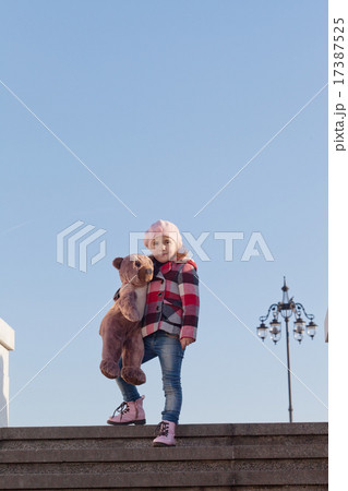 Girl with a big toy bear costs on a ladder 17387525