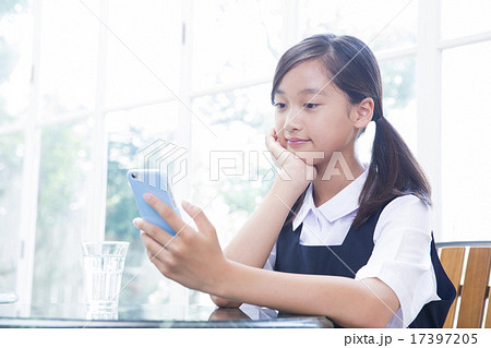 カフェでスマホを操作する制服姿の中学生の女の子の写真素材