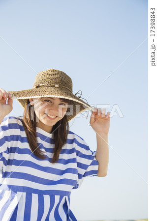 青空と麦わら帽子をかぶった笑顔の女性の写真素材