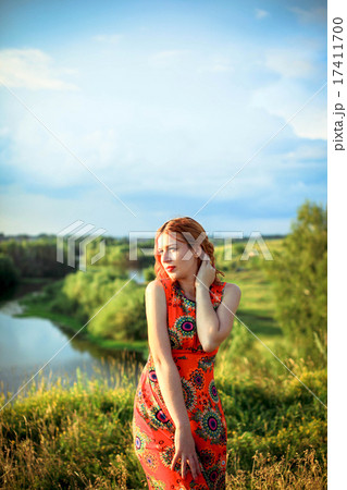 Young red-haired woman on the rock near river is fashionable poses in sunset time 17411700