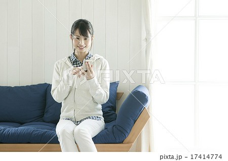ソファに座ってスマホを操作する若い女性の写真素材
