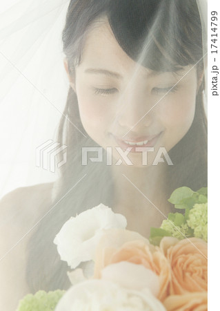 ブーケを持っている、ベールをかけたウェディングドレス姿の若い女性 17414799