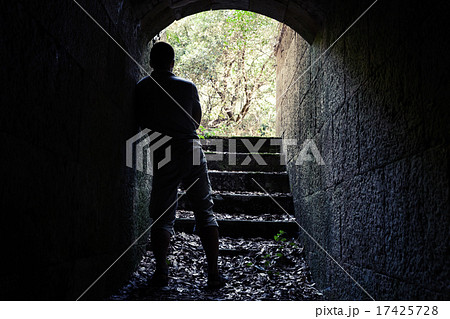Man stands in dark stone tunnel with glowing end 17425728