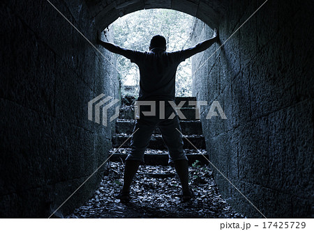 Man stands in dark stone tunnel with glowing end 17425729