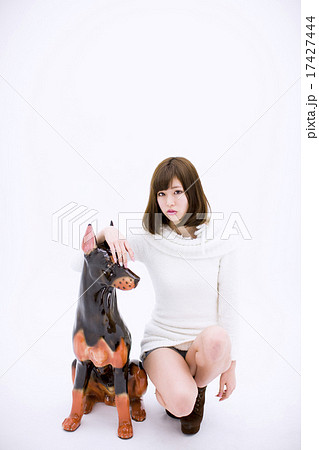 白い背景の前で陶器の犬の置物の横にしゃがみ込む白い服の若い女性の写真素材
