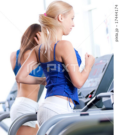 Two young women run on machine in the gym 17444174