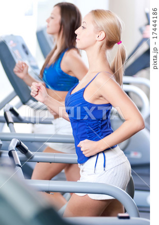 Two young women run on machine in the gym 17444186