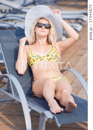 Young woman in swimsuit laying on chaise-longue poolside 17444875