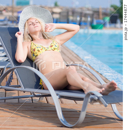 Young woman in swimsuit laying on chaise-longue poolside 17444877