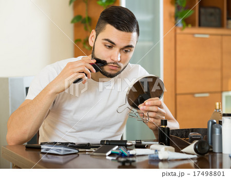 guy looking at mirror and shaving beard with trimmer 17498801