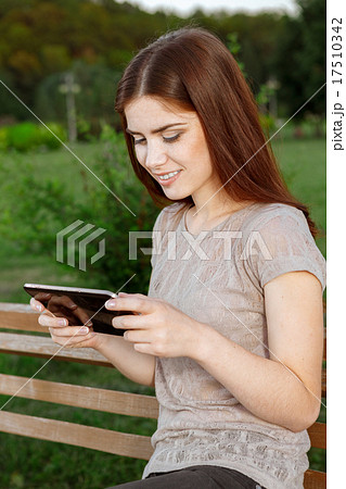 Young woman in a park texting on the tablet 17510342