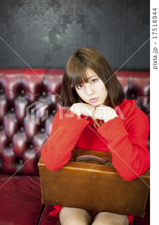 ワインレッド色の革張りのソファーに座って鞄に両肘をついているカメラ目線の若い女性 17518944