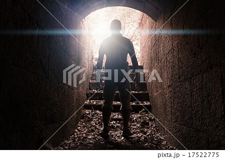 Man stands in dark stone tunnel with glowing end 17522775