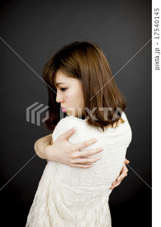 黒い背景の前で寂しげに自分自身を抱きしめている若い女性の写真素材