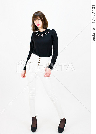 白い背景の前でカメラ目線で立っている白いパンツ ズボン 姿の若い女性の写真素材