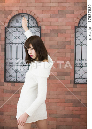 煉瓦造の壁の前で振り向きポーズをしている白いニットワンピースの 若い女性の写真素材