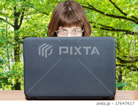 girl looks over cover of laptop and green forest 17647617
