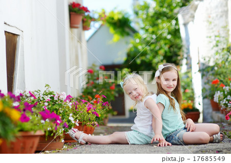 Two adorable little sisters sitting among flowers Two adorable little sisters sitting among flowers 17685549