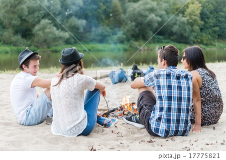 Young Adult Friends Hanging Around At Bonfire On Sandy Beach 17775821