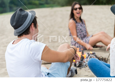 Young Adult Friends Hanging Around At Bonfire On Sandy Beach 17775822